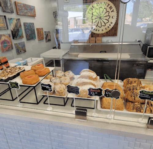 A display case filled with various pastries, including donuts, danishes, and sweet rolls, in a bright bakery setting.