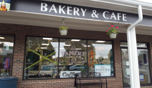 Exterior of a bakery and café named "The Pantry," featuring large windows and a welcoming "OPEN" sign.