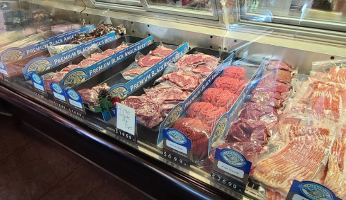 Display case filled with various cuts of premium black Angus beef, including steaks and ground beef, neatly packaged.