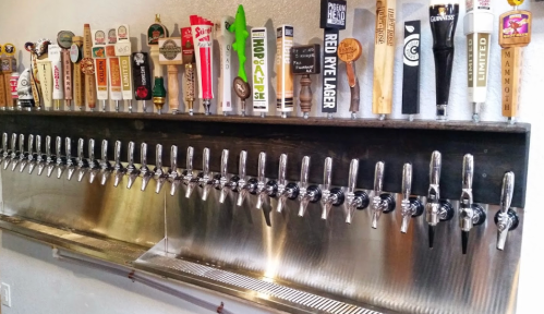 A wall-mounted beer tap system with numerous taps and handles, showcasing a variety of beer brands.