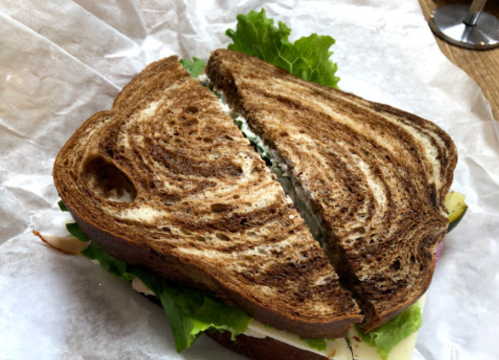 A sandwich with leafy lettuce and a creamy filling, made with two slices of swirled brown bread, cut in half.