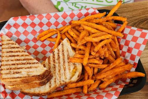 A basket with a grilled cheese sandwich and a side of crispy sweet potato fries on a checkered paper.