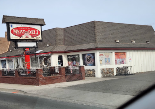 A corner deli with a sign reading "Meat & Deli," featuring outdoor seating and large windows.