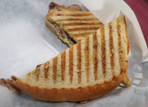 A toasted sandwich with grill marks, cut in half, resting on white parchment paper.