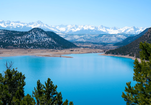 A serene lake surrounded by mountains, with clear blue water and a bright blue sky.
