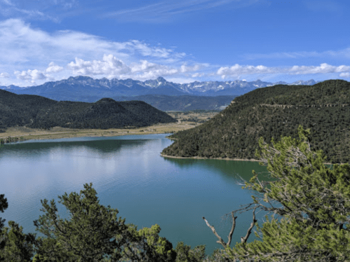 A serene lake surrounded by mountains and lush greenery under a clear blue sky.