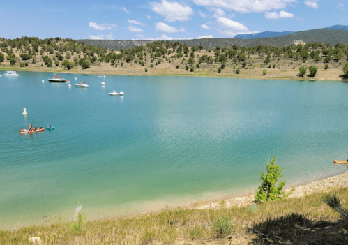 A serene lake surrounded by green hills, with boats on the water and a clear blue sky above.