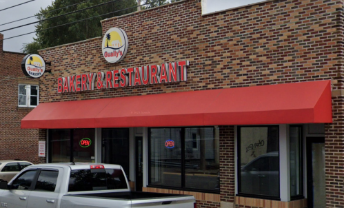 Exterior of Gualy’s Bakery & Restaurant, featuring a red awning and large signage, with a white truck parked outside.