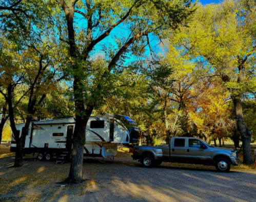 A gray truck towing a large RV parked under colorful autumn trees.