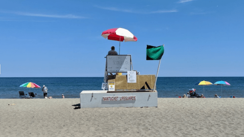 A lifeguard station on a sandy beach with colorful umbrellas and a clear blue sky in the background.