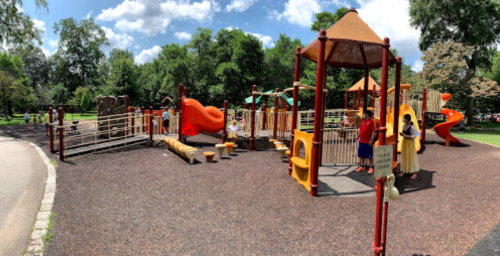 A colorful playground with slides, climbing structures, and children playing under a blue sky with fluffy clouds.