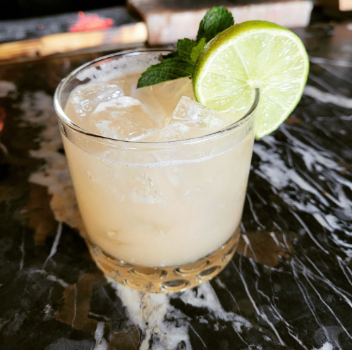 A refreshing cocktail with ice, garnished with a lime slice and mint, served in a clear glass on a marble surface.