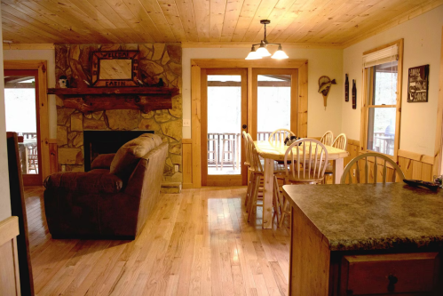 Cozy cabin interior featuring a stone fireplace, dining area, and wooden furnishings with natural light.