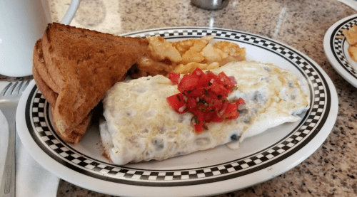 A plate with a cheese omelette topped with diced tomatoes, toast, and hash browns on a checkered rim.
