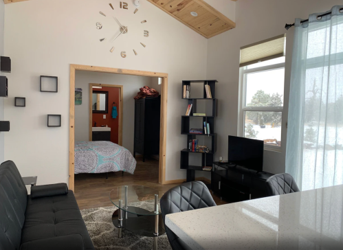 Cozy living space with a sofa, bookshelf, and TV, leading to a bedroom with a colorful quilt and snowy view outside.