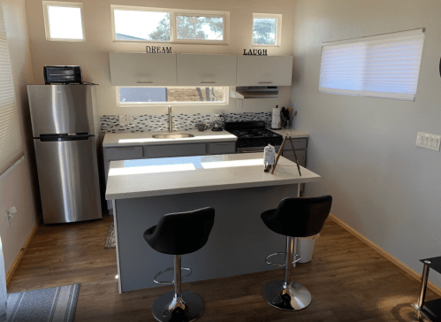 Modern kitchen with gray cabinets, stainless steel appliances, and a central island with two black bar stools.