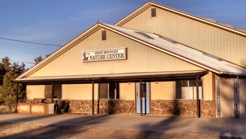 Exterior of the White Mountain Nature Center, featuring a beige building with a stone base and a blue door.