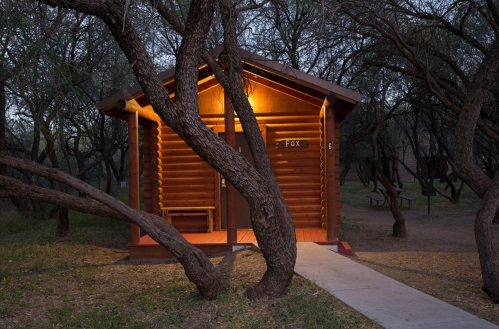 A cozy log cabin with a warm light, surrounded by trees in a serene outdoor setting at dusk.