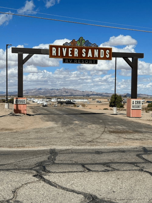 Sign for River Sands RV Resort at the entrance, with mountains and blue sky in the background.