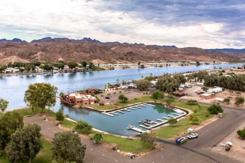 Aerial view of a river with a marina, surrounded by trees and mountains under a cloudy sky.