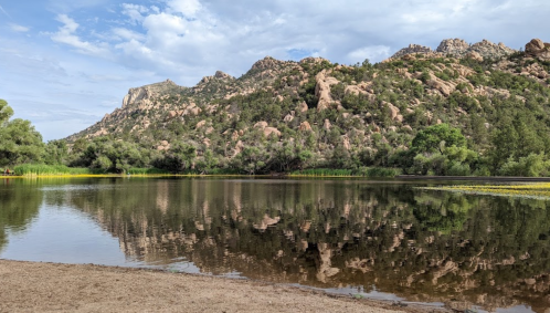 A serene lake reflecting rocky hills and greenery under a partly cloudy sky.