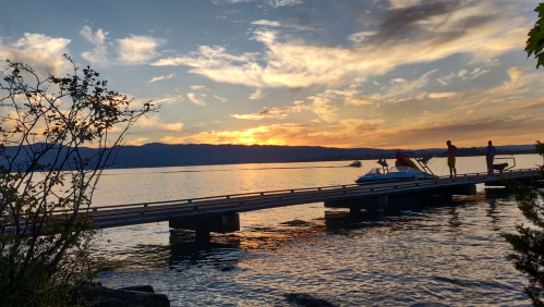 Silhouetted figures on a dock at sunset, with calm water and colorful clouds reflecting in the sky.