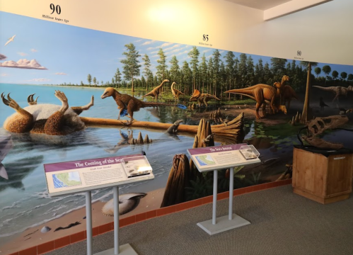 A mural depicting dinosaurs near a lake, with informational displays in a museum setting.