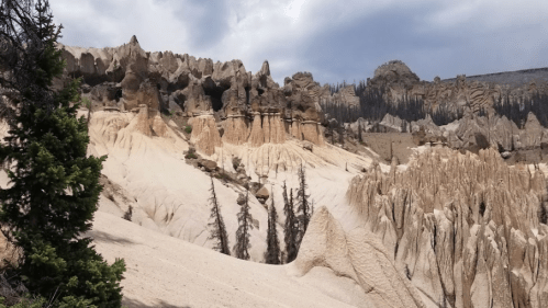 A rugged landscape featuring unique rock formations and sparse trees under a cloudy sky.