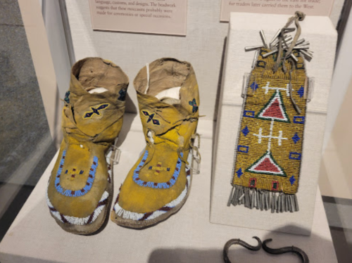 Traditional Native American moccasins and a beaded pouch displayed in a museum exhibit.
