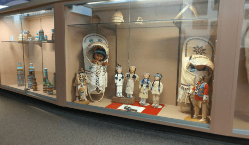 Display case featuring traditional Native American dolls and artifacts, showcasing cultural craftsmanship and heritage.