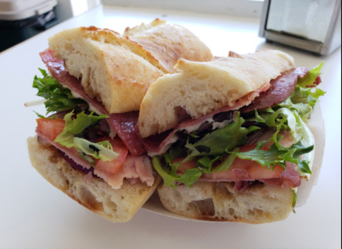 A close-up of two sandwiches stacked, filled with lettuce, tomato, and layers of meat on crusty bread.