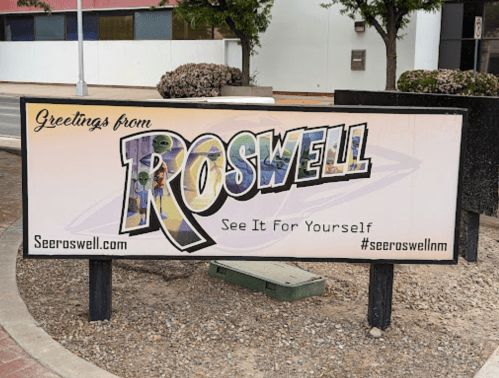 Sign welcoming visitors to Roswell, featuring colorful graphics and the text "See It For Yourself."