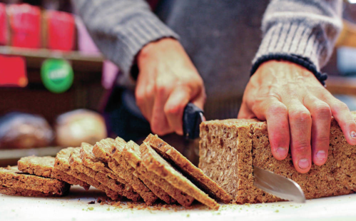 A person slices a loaf of brown bread on a cutting board with a knife.