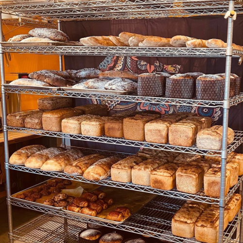 A display of various freshly baked breads and pastries on metal shelves in a bakery.