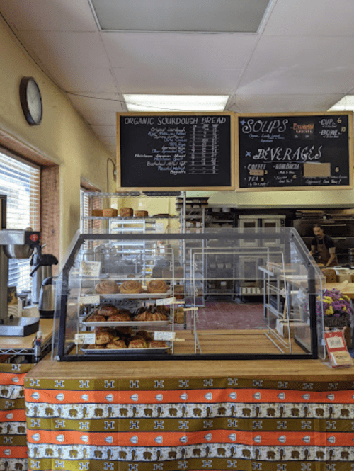 A cozy bakery interior featuring a display case with pastries and a chalkboard menu listing soups and beverages.