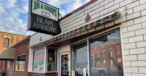 Exterior of Jim & Connie's Blair Bakery, featuring a sign and awning, with a cloudy sky in the background.