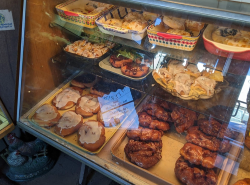A display case filled with various baked goods, including cinnamon rolls and pastries, in a cozy bakery setting.
