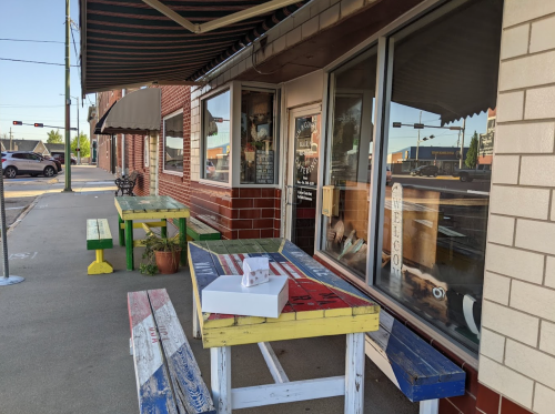 Colorful outdoor tables in front of a shop, with a white box on one table and a street view in the background.