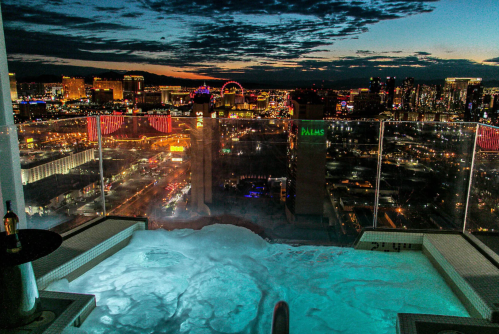 A luxurious hot tub on a balcony overlooking the vibrant Las Vegas skyline at sunset.