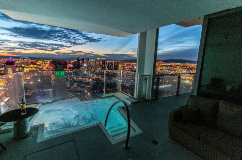 A luxurious balcony with a hot tub overlooking a vibrant city skyline at dusk.