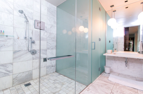 Modern bathroom featuring a glass shower, marble tiles, and a sleek vanity with round light fixtures.