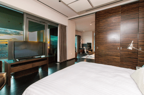 Modern bedroom with a large window, wooden furniture, a TV, and a view of the sunset.