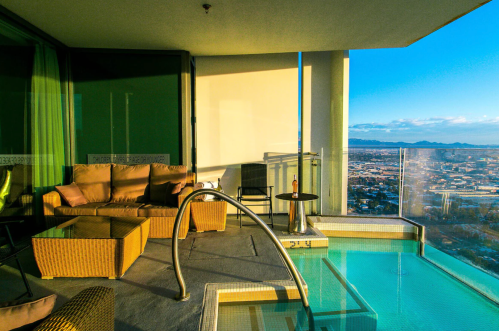 A stylish balcony with a hot tub, seating area, and a panoramic view of the city and mountains in the background.