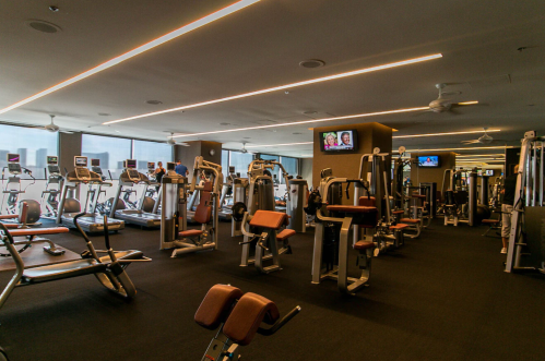 A modern gym interior with various exercise machines and equipment, featuring large windows and overhead lighting.