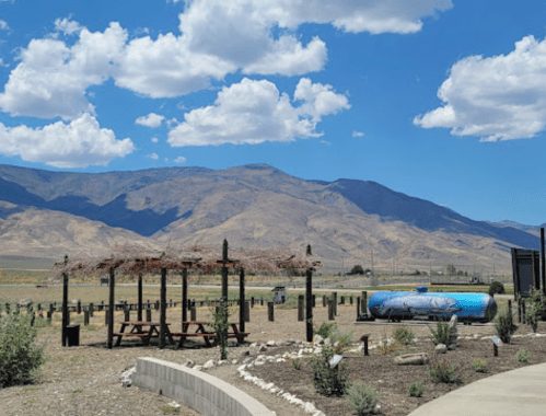 A scenic view of mountains under a blue sky with clouds, featuring a picnic area and a blue water tank in the foreground.