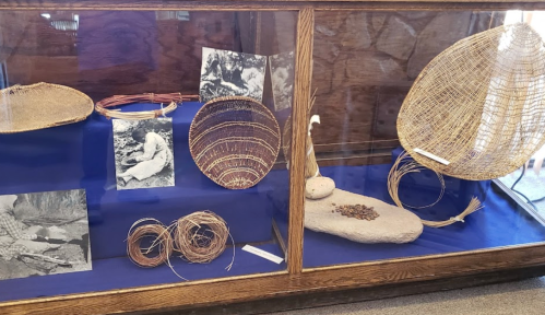 Display case featuring woven baskets, artifacts, and historical photographs on a blue background.