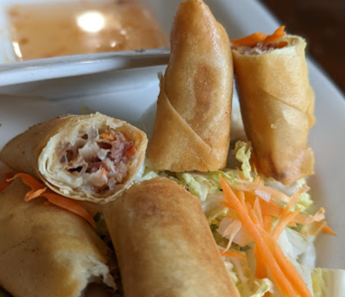 A close-up of crispy spring rolls on a plate, with one cut open, revealing a savory filling and garnished with vegetables.