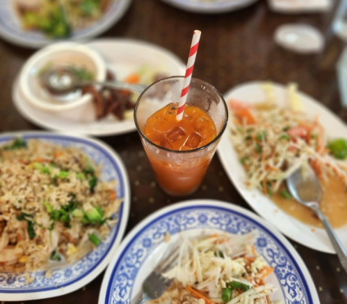A table set with various dishes, including salads and fried rice, alongside a glass of iced drink with a striped straw.