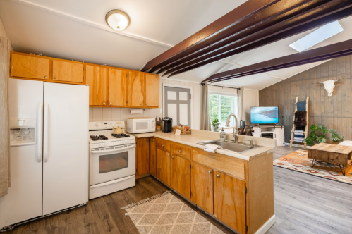Bright kitchen with wooden cabinets, white appliances, and a cozy living area featuring a TV and decorative elements.