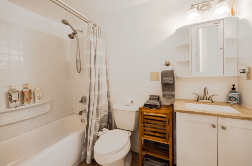 A clean, modern bathroom featuring a bathtub, shower, sink, and wooden storage unit with towels.